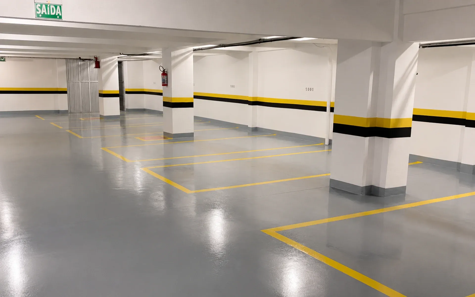Estacionamento subterrâneo com piso epóxi Hazzin cinza claro RAL 7035 e demarcação amarela das vagas após aplicação